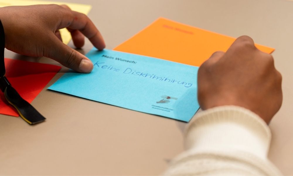 Ein junger Mensch mit dunkler Hautfarbe schreibt auf eine blaue Karte: keine Diskriminierung.