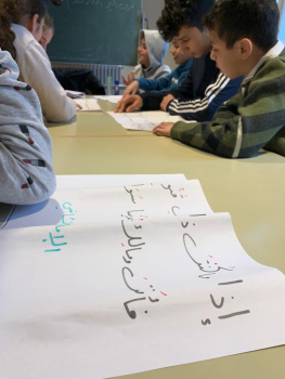 mehrere Kinder sitzen vor großen Papieren mit arabischen Schriftzeichen