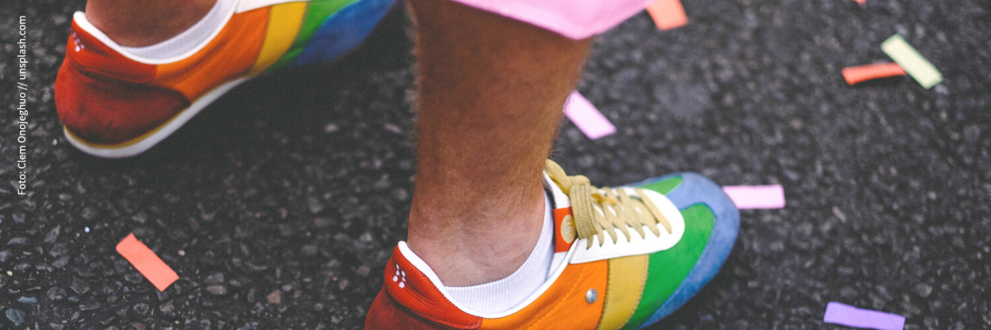 ein Mensch trägt Schuhe in Regenbogenfarben, auf der Straße liegt Konfetti