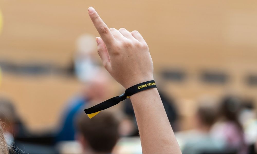Eine junge Frau meldet sich zu Wort. Sie trägt ein Armband auf dem steht "Deine Freiheit"