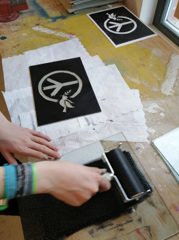 Eine Person Druck ein Motiv mit dem Friedenssymbol und der Friedenstaube auf ein Papier