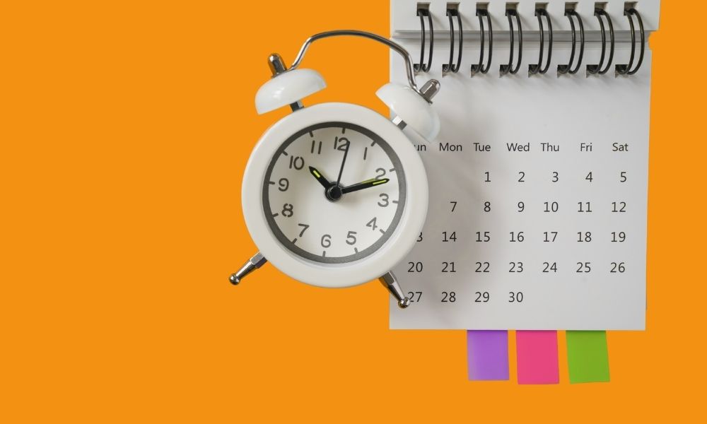Auf orangenem Hintergrund sind ein Kalenderblatt und ein weißer Wecker abgebildet.